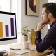 Man reviewing a four-bar comparison chart on a monitor in a bright workspace